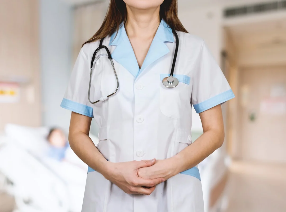 A confident female nurse in fitted FIGS scrubs and Dansko clogs reviewing a stethoscope at a busy hospital nursing station